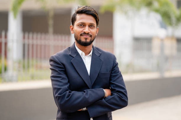 Outdoor Portrait of young businessman wearing formal dress and looking at camera in downtown area of modern metropolis.